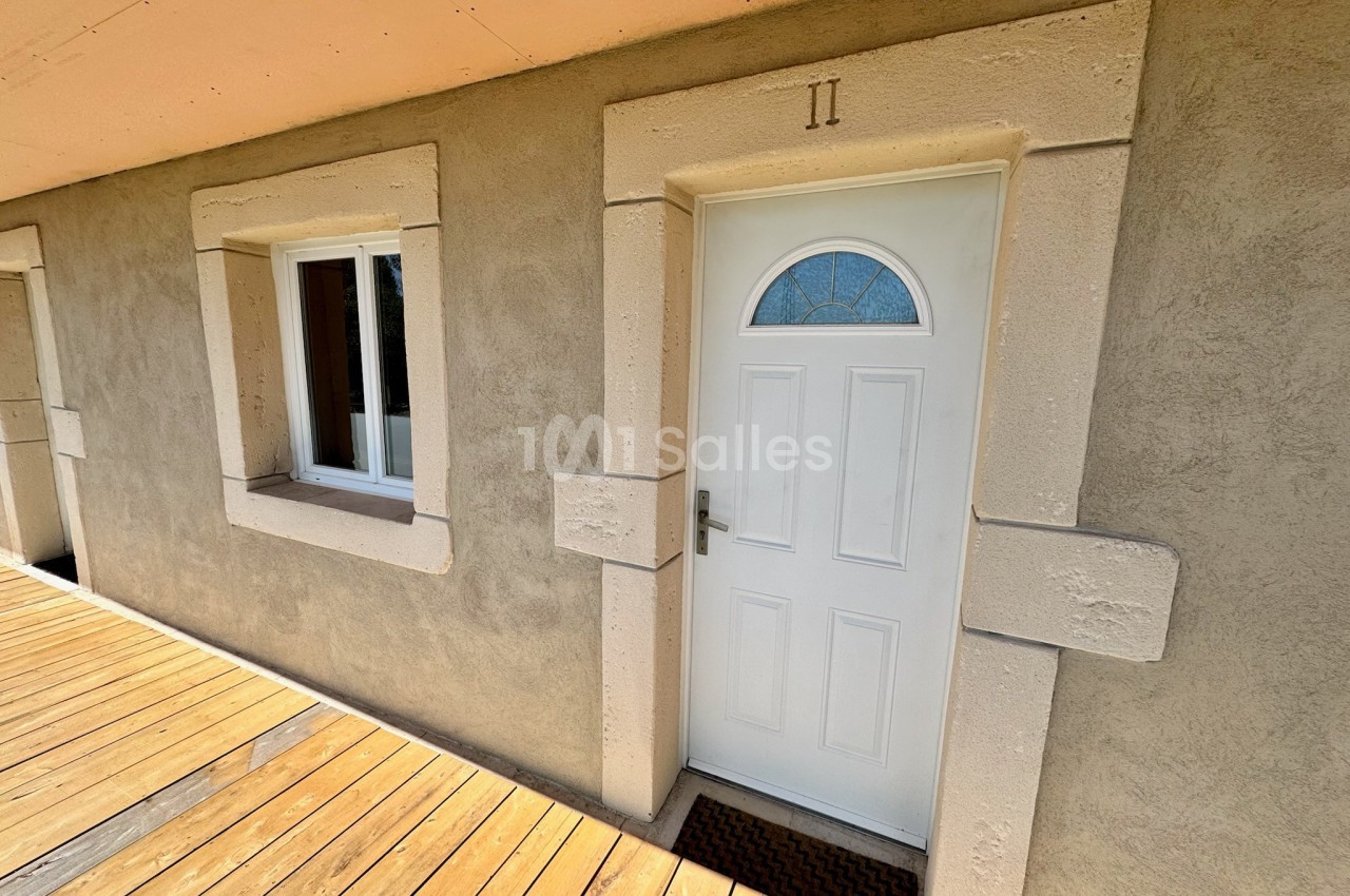 Porte blanche avec fenêtre semi-circulaire et encadrement en pierre, à côté d'une fenêtre sur une façade beige.