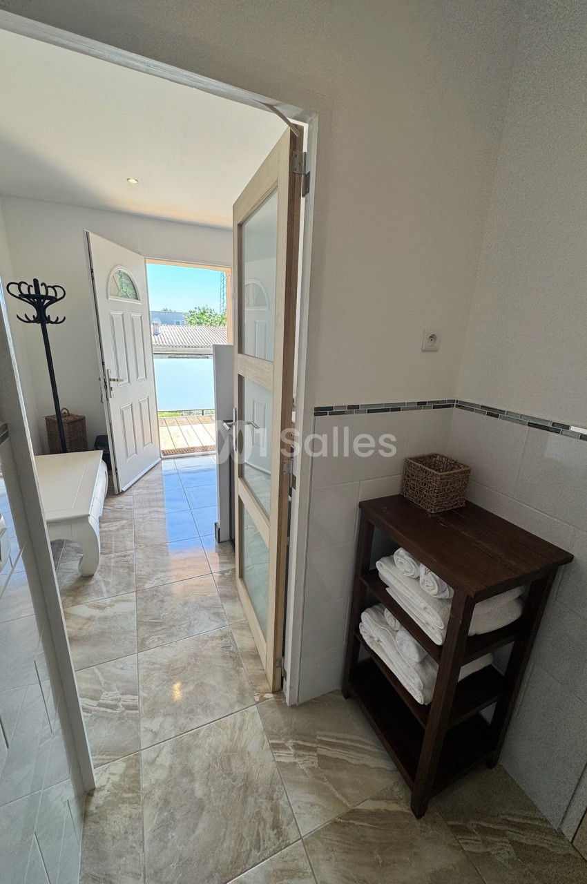 Salle de bain lumineuse avec étagère en bois, serviettes pliées et porte ouverte sur une terrasse ensoleillée.
