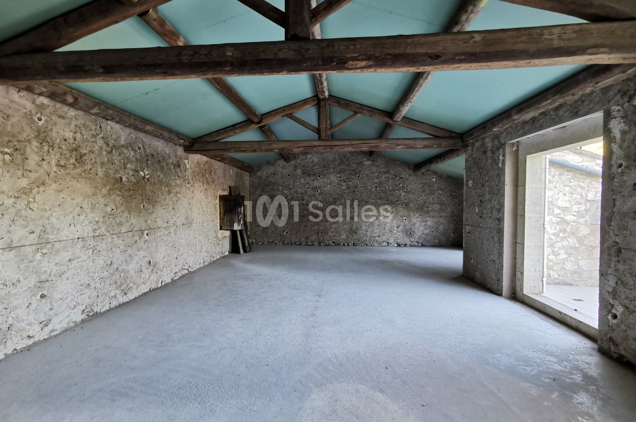 Intérieur d'une pièce vide avec murs en pierre, plafond en bois et ouvertures laissant entrer la lumière naturelle.