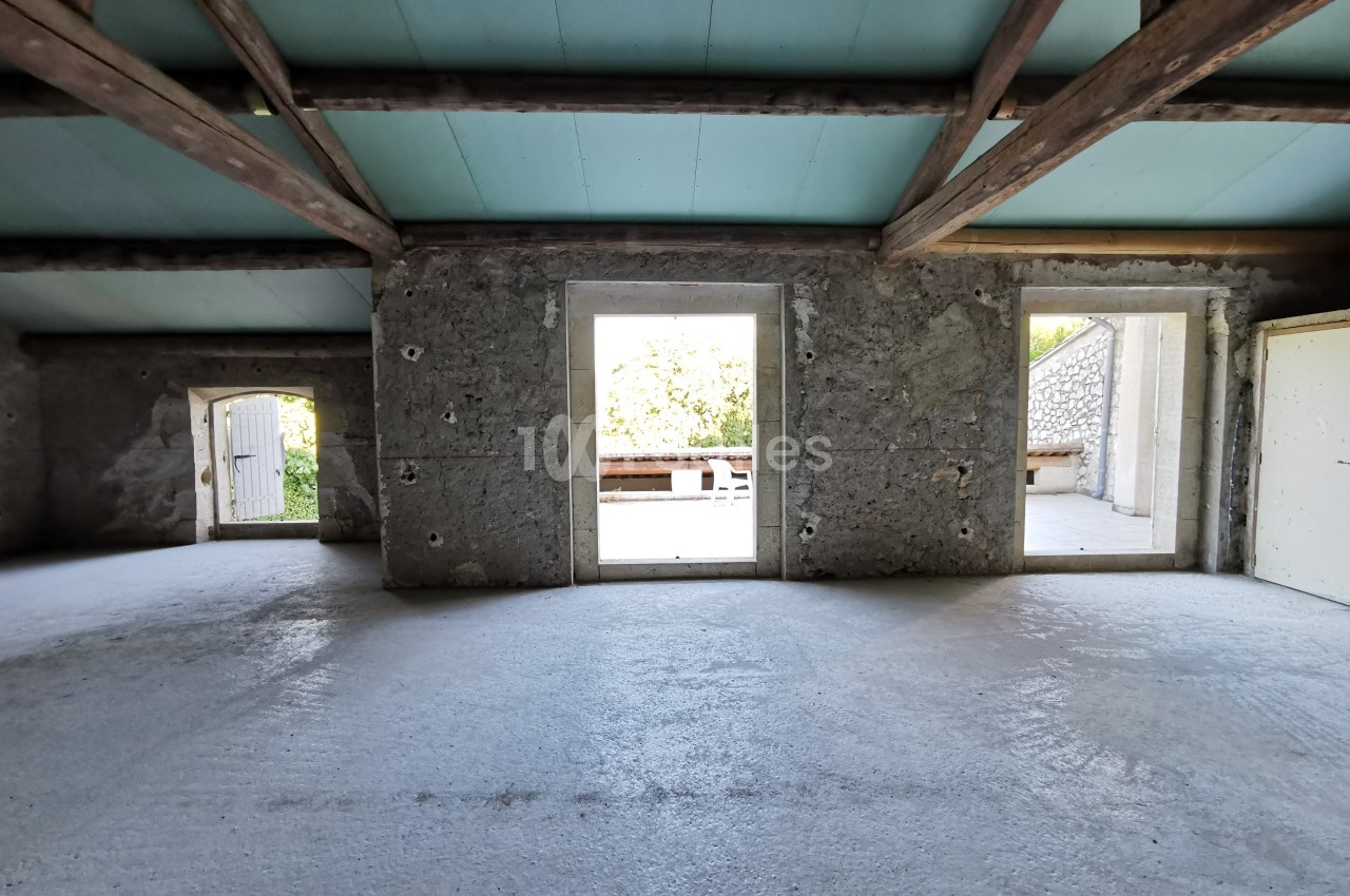 Intérieur d'une pièce vide avec murs en pierre, plafond en bois et ouvertures donnant sur un extérieur lumineux.