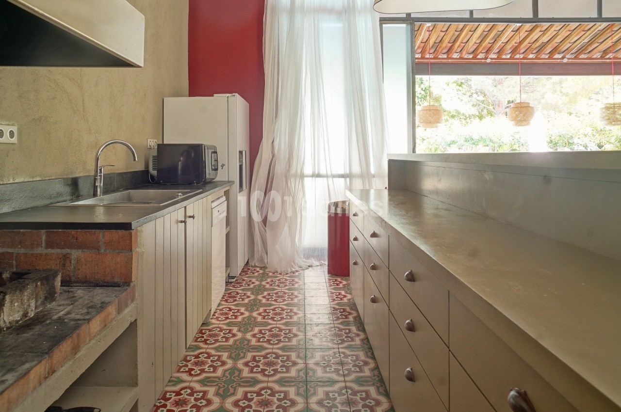 Cuisine lumineuse avec plan de travail en bois, évier en inox, micro-ondes et sol en carreaux colorés.