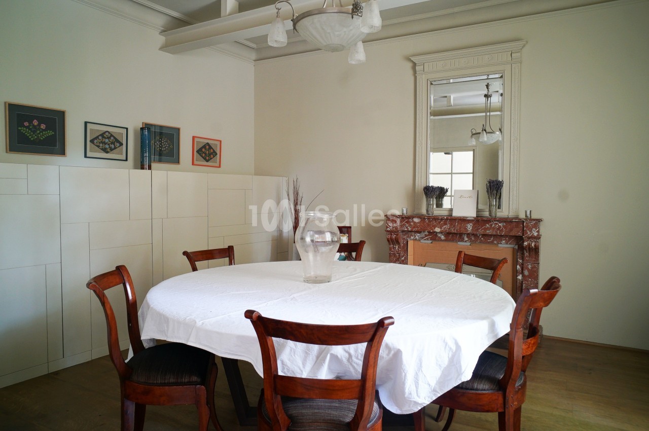 Salle à manger avec table ronde couverte d'une nappe blanche, chaises en bois, cheminée en marbre et miroir mural.