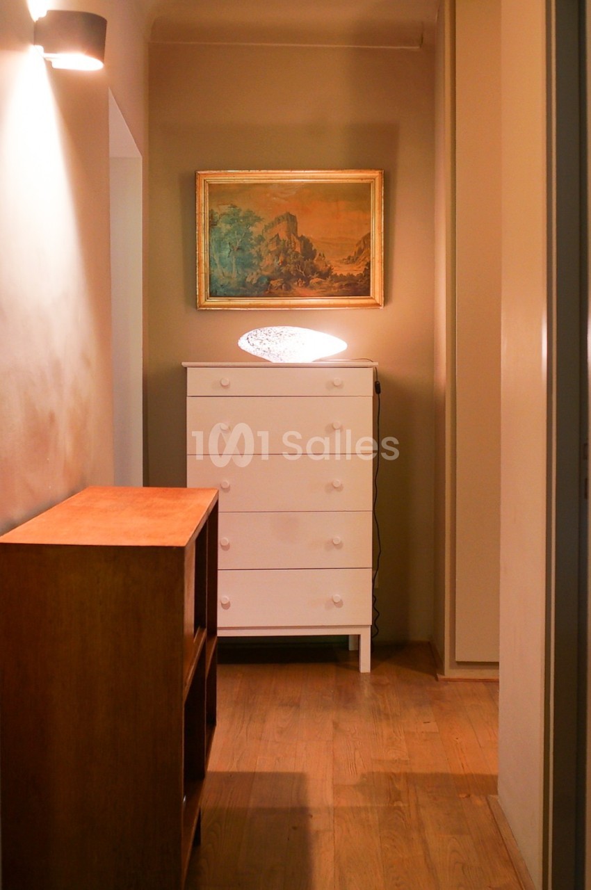 Couloir étroit avec parquet, commode blanche, lampe allumée, tableau encadré et meuble en bois.