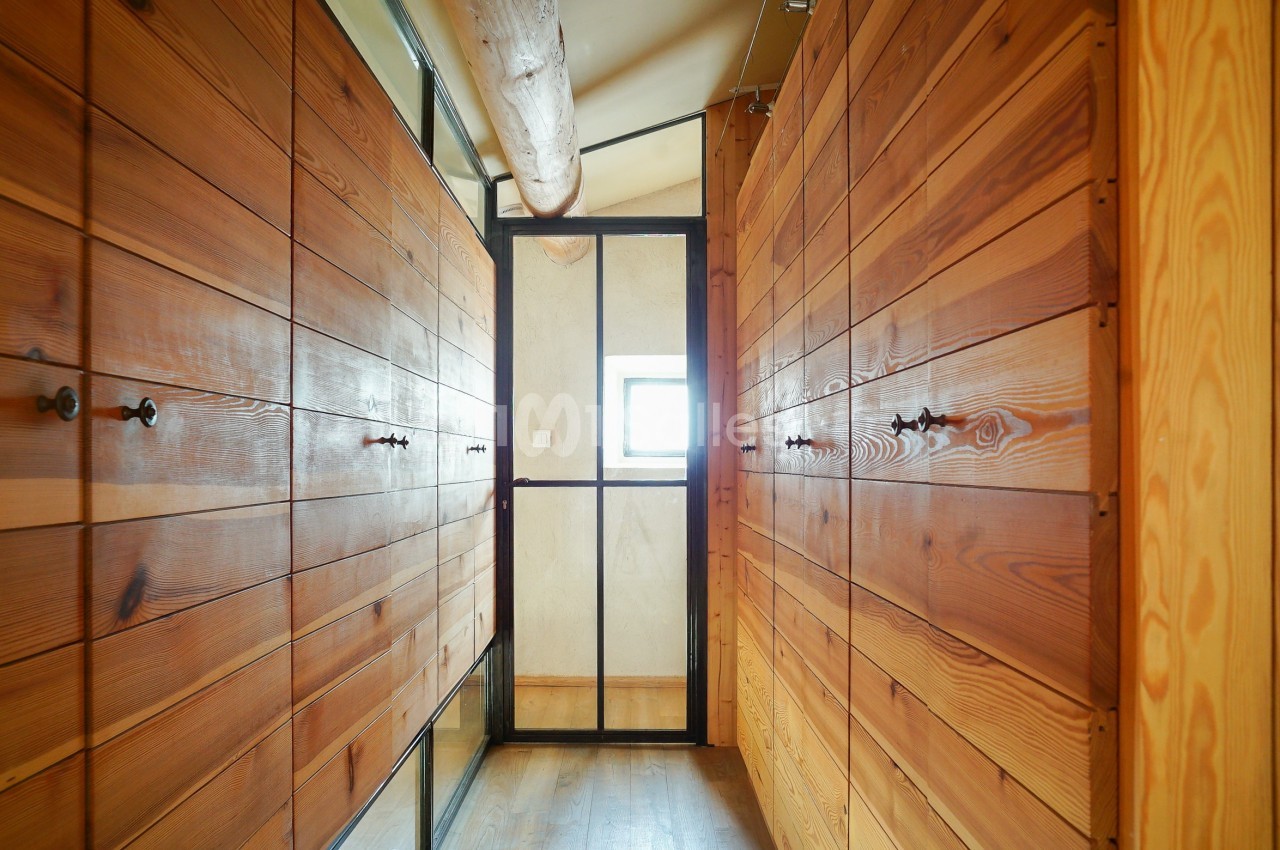 Couloir étroit avec des murs en bois, une porte vitrée noire et une petite fenêtre laissant entrer la lumière.