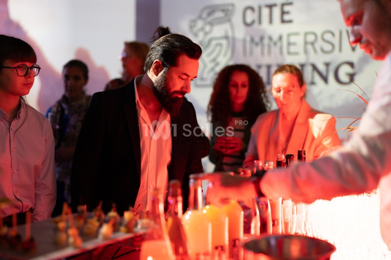 Un homme observe un buffet éclairé en rouge lors d'un événement avec des participants en arrière-plan.