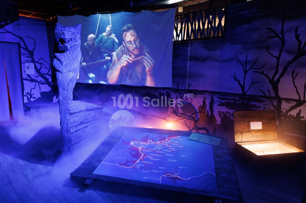 Scène immersive avec carte éclairée au sol, projection d'un homme, décor sombre et brumeux, ambiance mystérieuse.