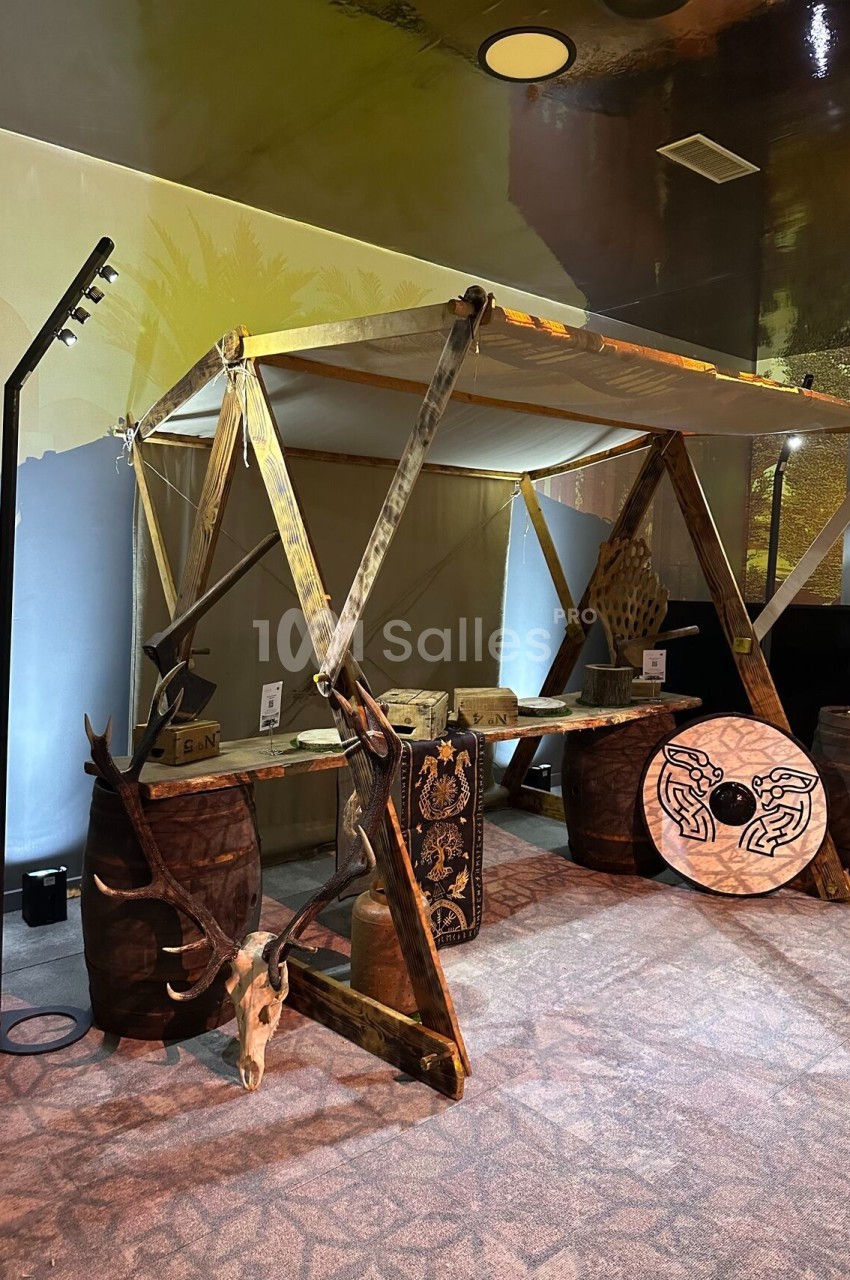 Stand en bois avec une structure en toile, décoré de tonneaux, crânes d'animaux et motifs gravés, dans un espace intérieur.