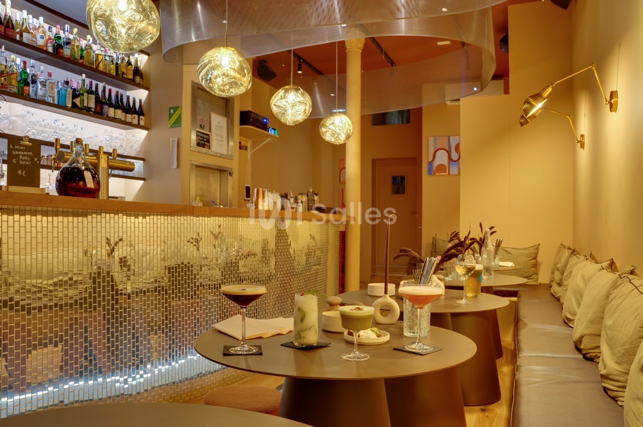 Intérieur d'un bar moderne avec tables basses, cocktails variés, éclairage chaleureux et décoration contemporaine.