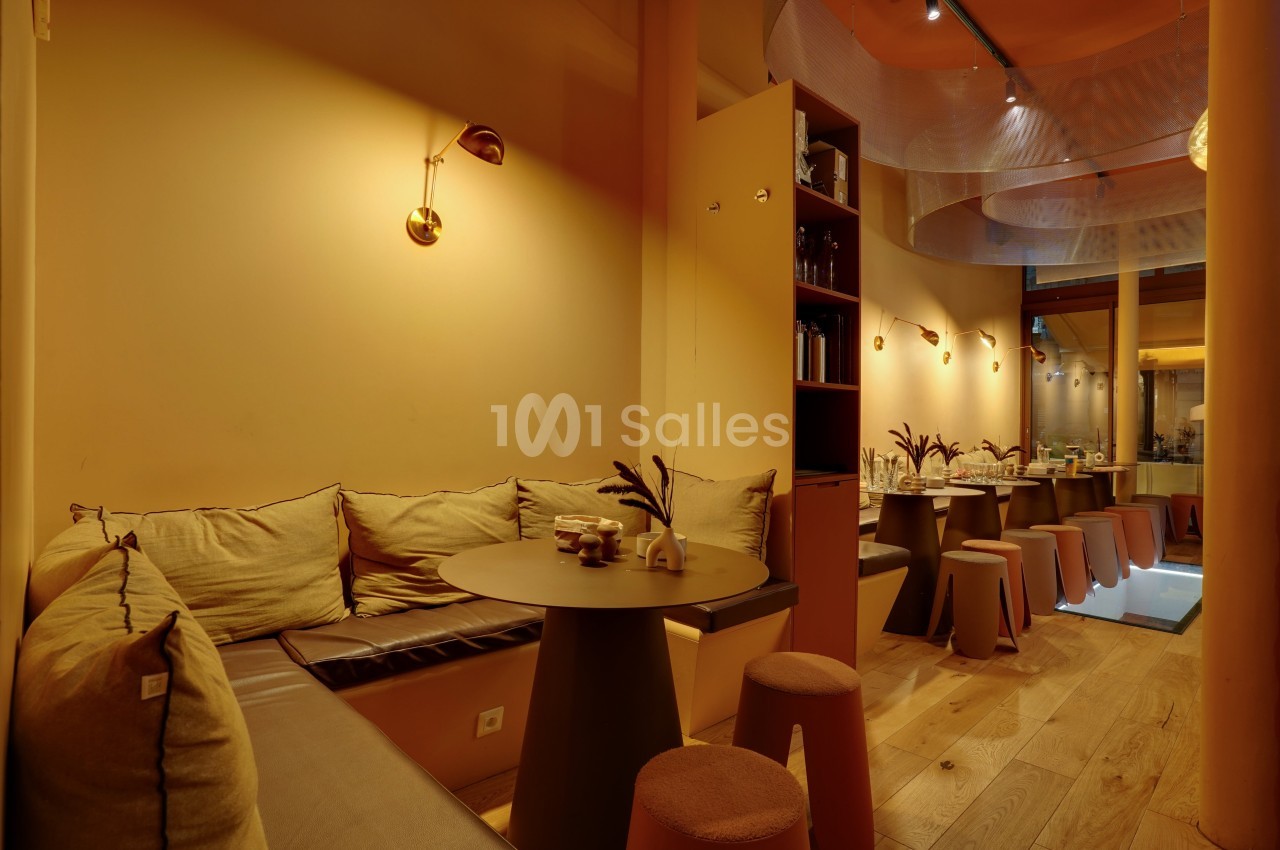 Salle de restaurant chaleureuse avec banquettes, tables rondes, tabourets et éclairage tamisé.