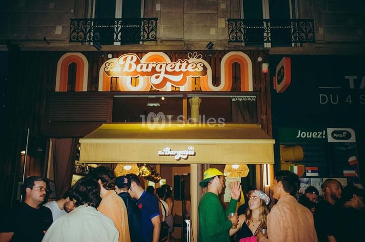 Groupe de personnes discutant devant une devanture de restaurant éclairée en soirée.