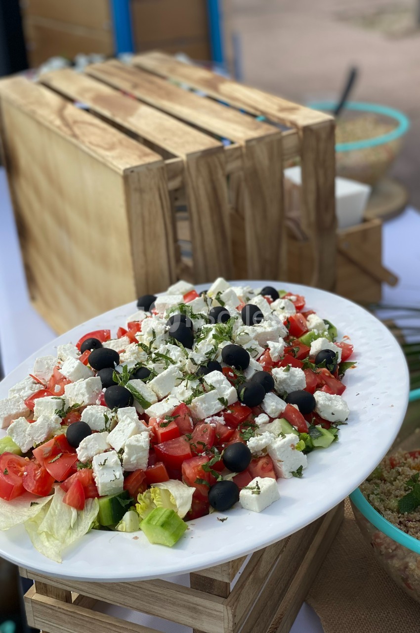 Assiette de salade grecque avec feta, tomates, concombres, olives noires et herbes, présentée sur une table en extérieur.