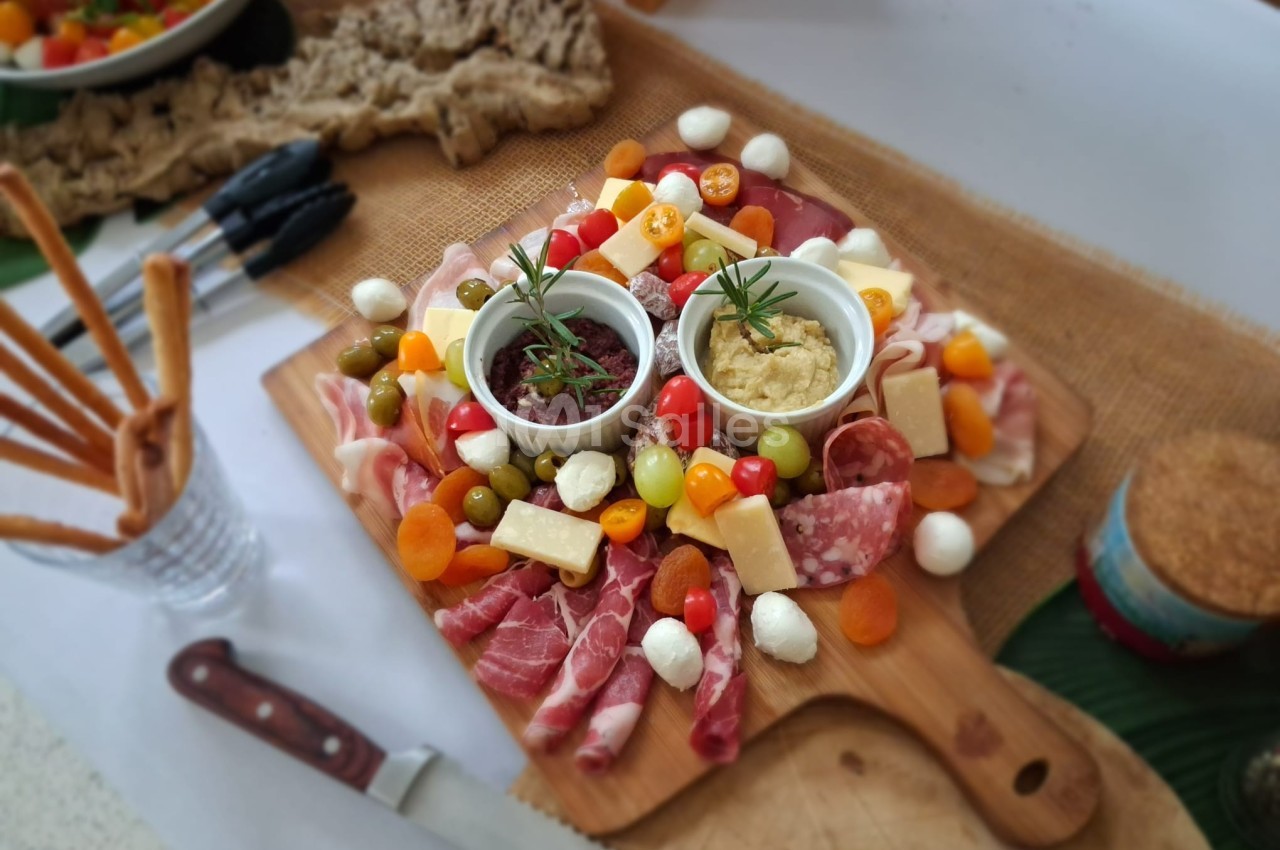 Plateau de charcuterie avec fromages, olives, tomates cerises, dips et grissini, présenté sur une planche en bois.