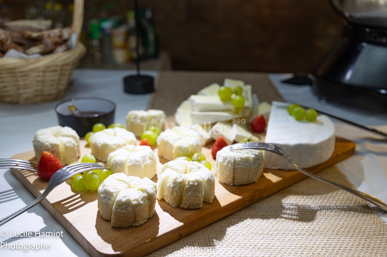 Plateau de fromages variés avec raisins et fraises, présenté sur une table éclairée dans un cadre convivial.