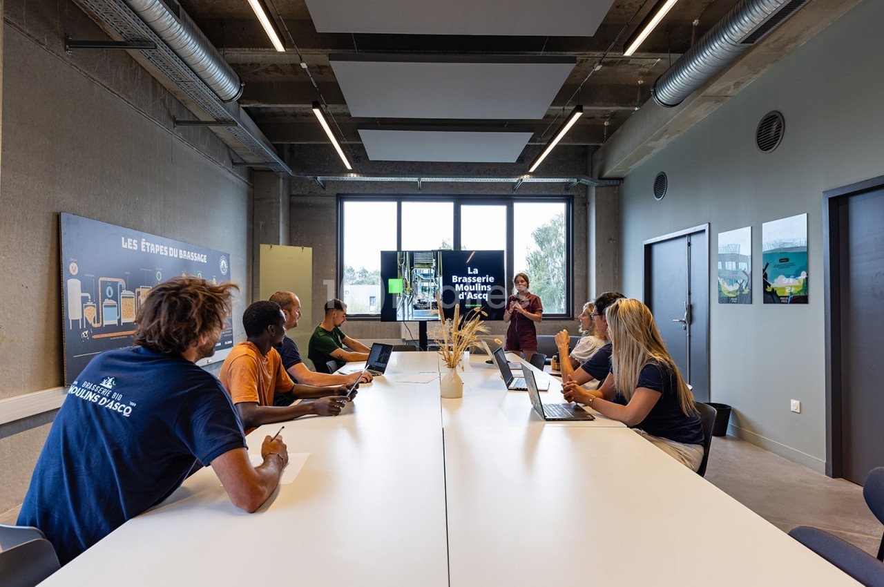 Des personnes assises autour d'une table en réunion dans une salle moderne avec un écran de présentation.