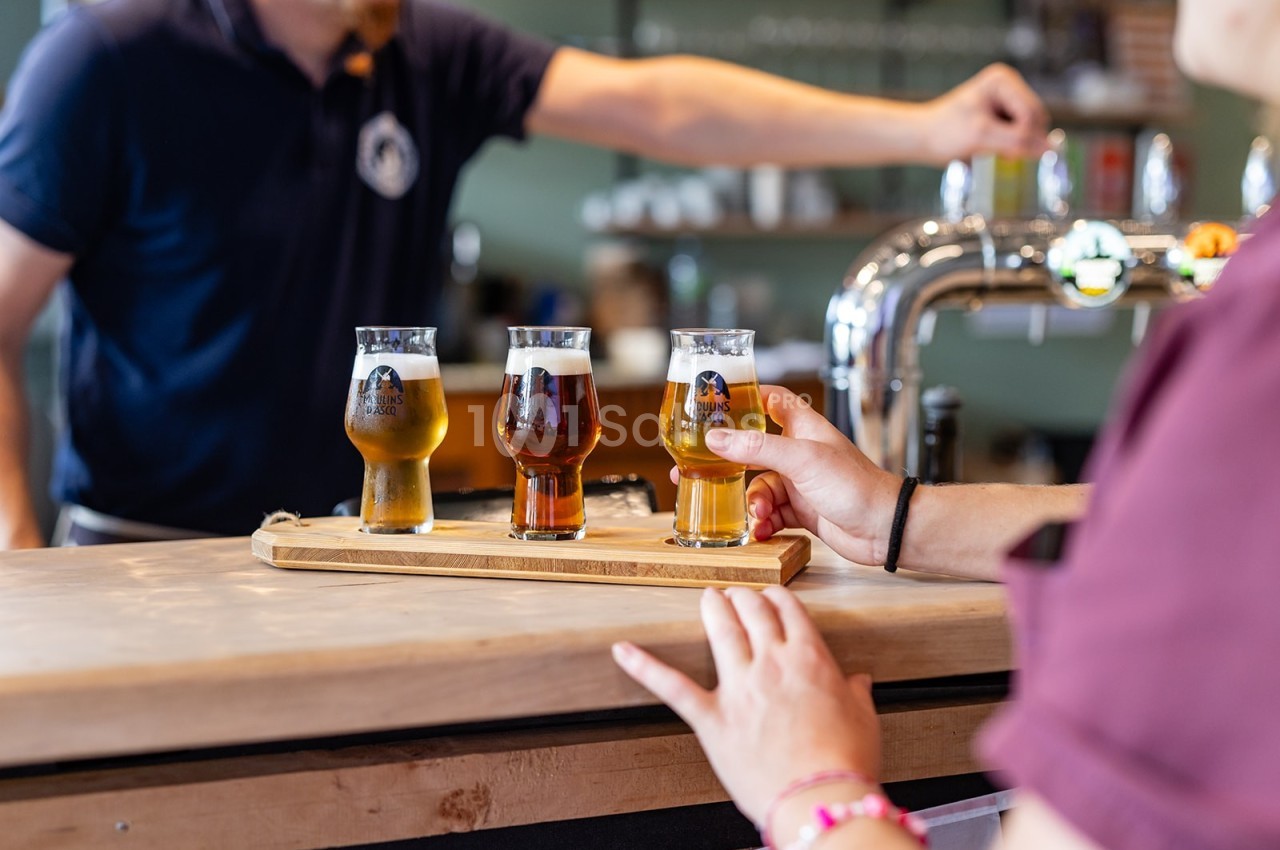 Une personne sert un plateau de dégustation avec trois verres de bière sur un comptoir de bar.
