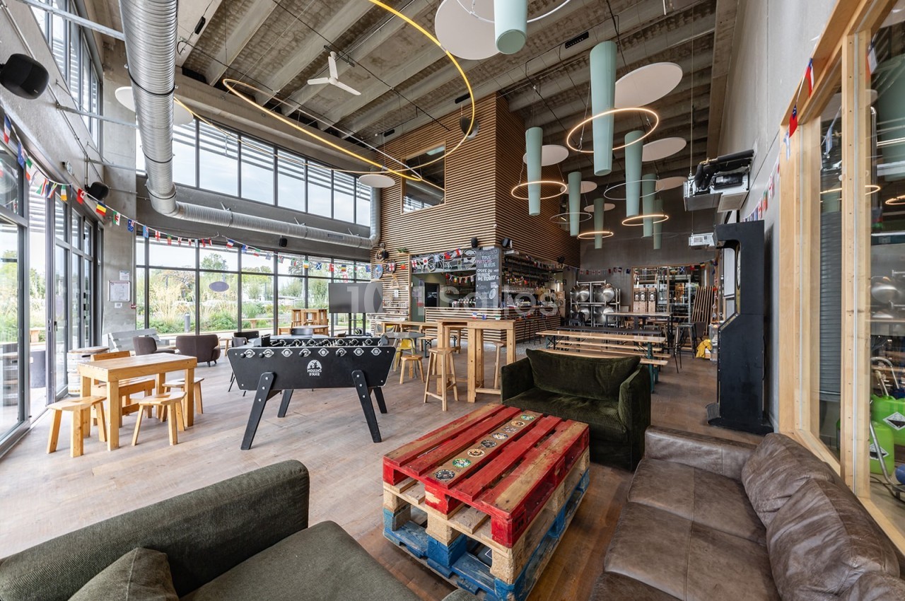 Intérieur d'un café moderne avec des tables en bois, un baby-foot, des canapés et une décoration colorée.