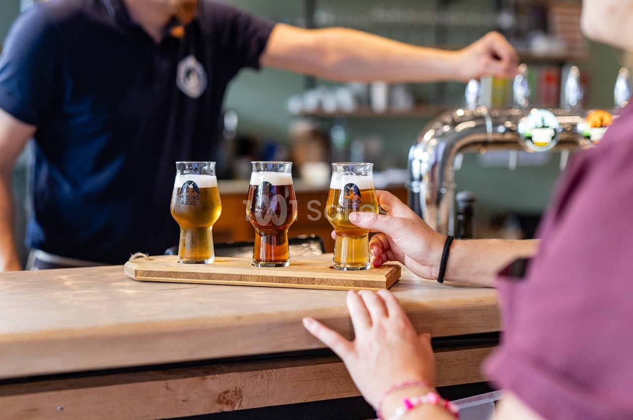 Une personne sert un plateau de dégustation avec trois verres de bière sur un comptoir de bar.
