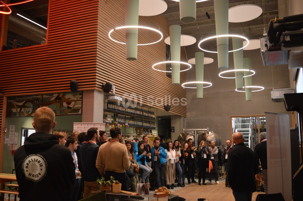 Un groupe de personnes rassemblées dans un espace moderne avec des luminaires suspendus et des étagères de bouteilles.