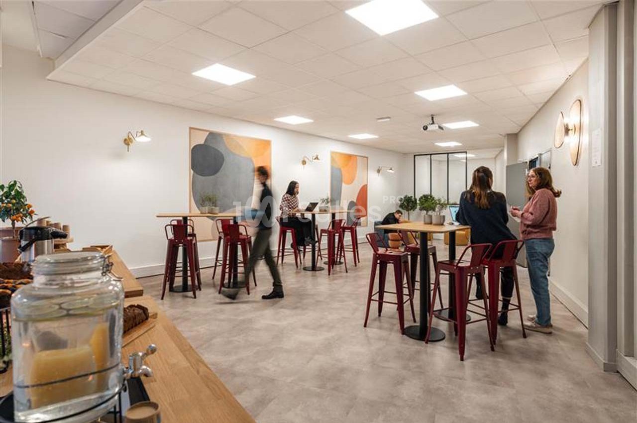 Espace de coworking lumineux avec tables hautes, chaises rouges, décorations murales et personnes discutant.