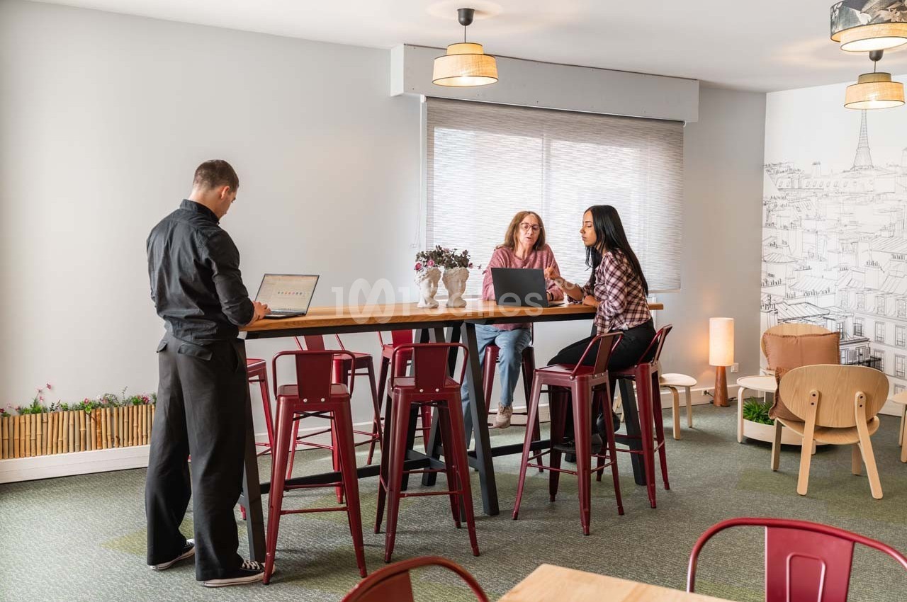 Trois personnes travaillent et discutent autour d'une table haute dans un espace lumineux et aménagé.