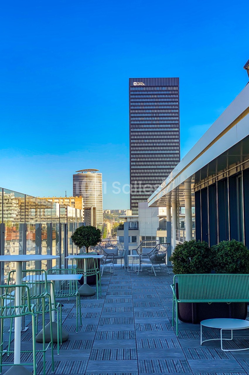 Terrasse aménagée avec mobilier vert, offrant une vue sur des immeubles modernes et un ciel dégagé.