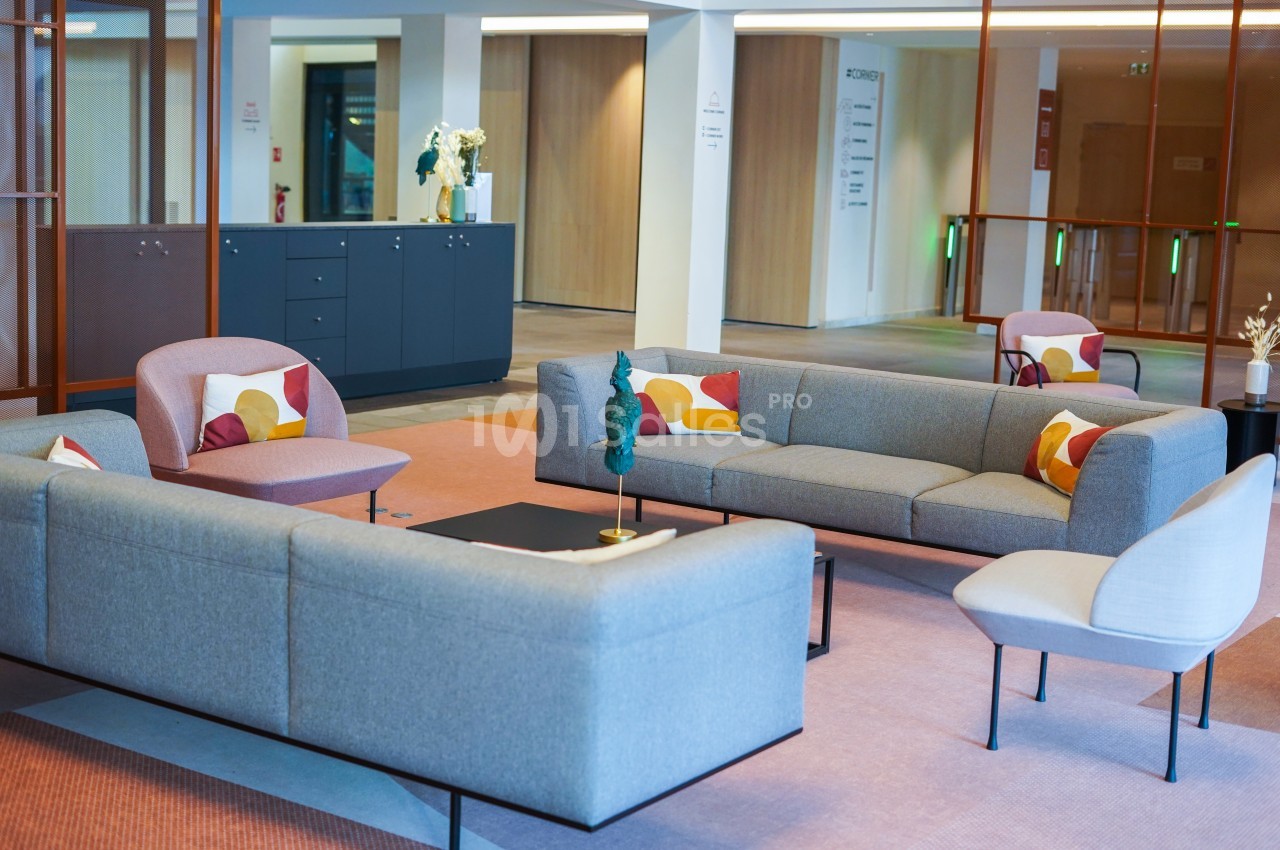 Espace salon moderne avec canapés gris, fauteuils colorés et table basse dans un intérieur lumineux.