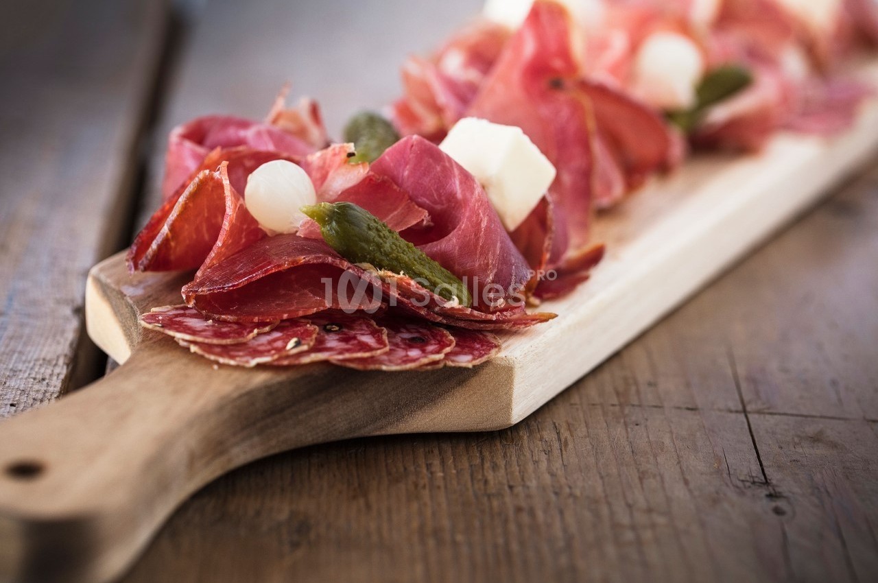 Planche en bois garnie de charcuterie, cornichons, oignons marinés et cubes de fromage.