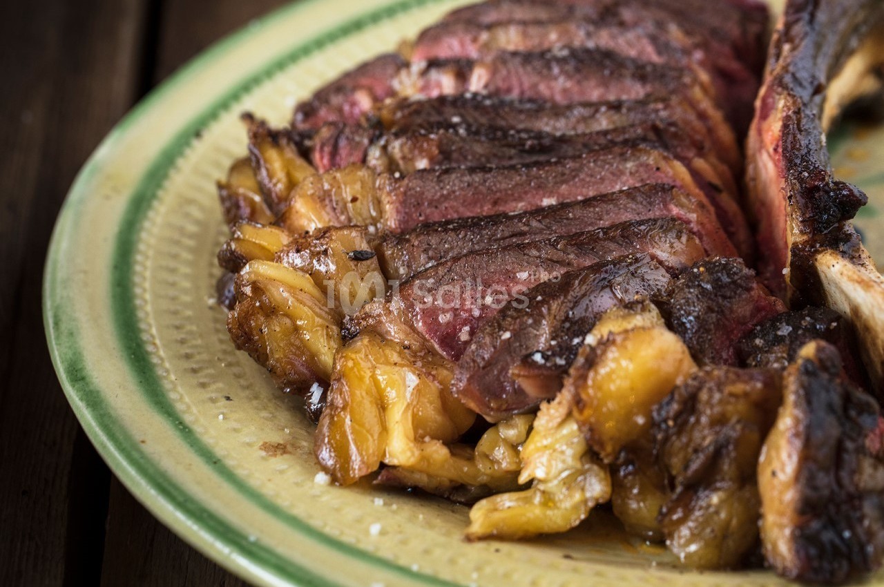 Tranche de viande grillée juteuse et marbrée, servie sur une assiette en céramique beige.