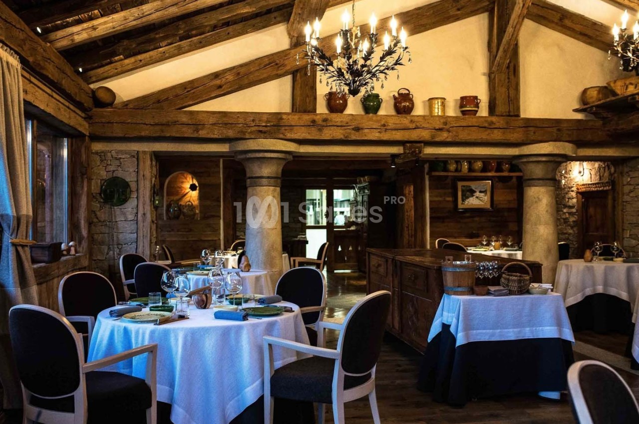 Salle de restaurant rustique avec poutres apparentes, tables dressées et ambiance chaleureuse.