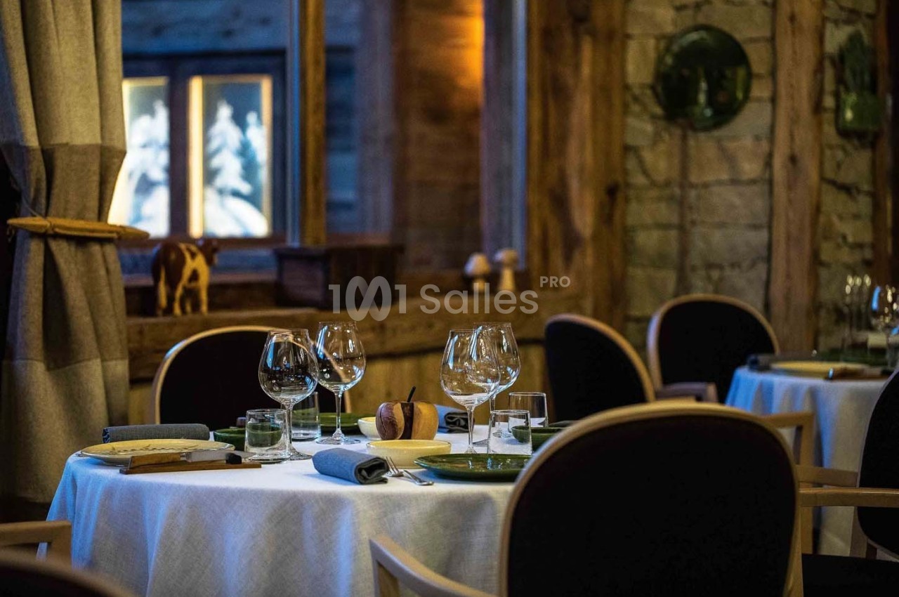 Salle de restaurant élégante avec tables dressées, nappes blanches, verres à pied et ambiance chaleureuse en bois.