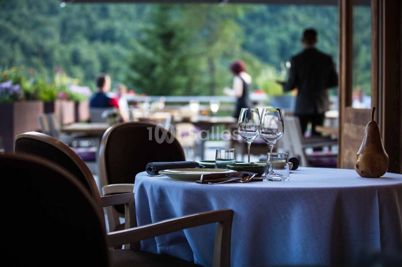 Table dressée avec des verres et des assiettes sur une terrasse de restaurant, avec vue sur un paysage verdoyant.