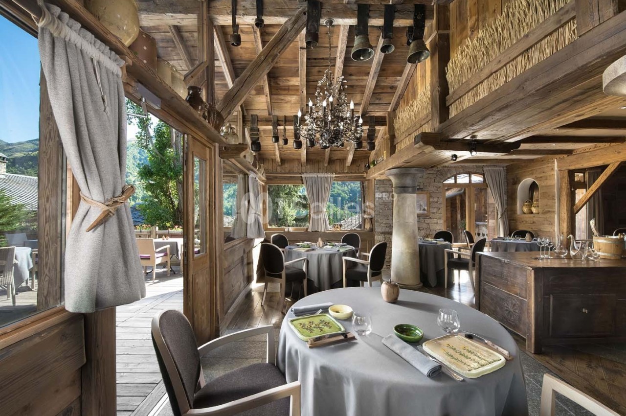 Salle de restaurant en bois avec grandes baies vitrées, tables dressées et vue sur un paysage montagneux.