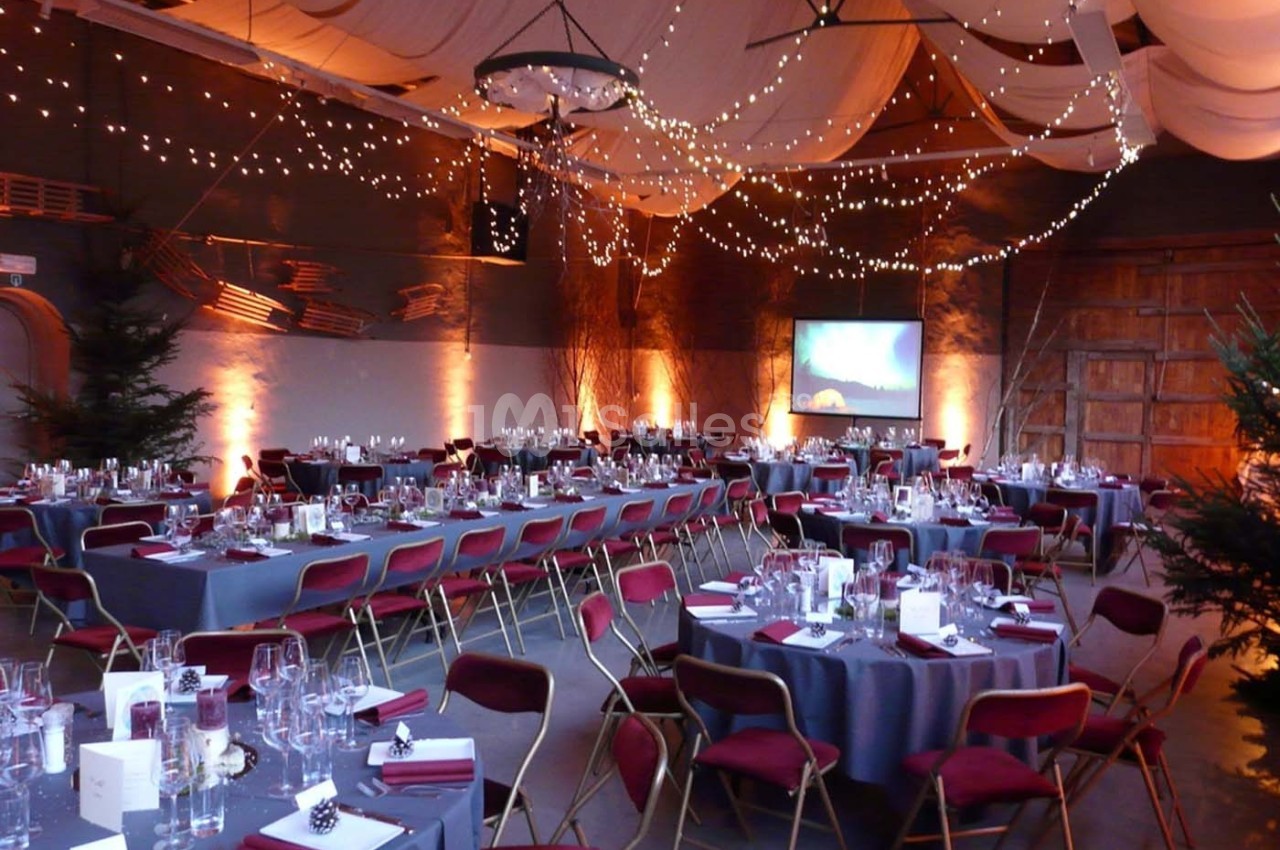 Salle de réception décorée avec des guirlandes lumineuses, des tables dressées et des chaises rouges.
