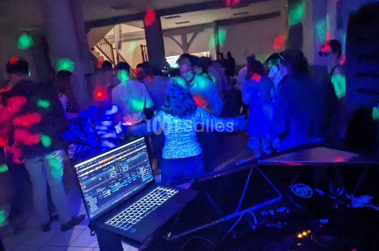 Personnes dansant dans une salle sombre éclairée par des lumières colorées, avec un ordinateur de DJ au premier plan.
