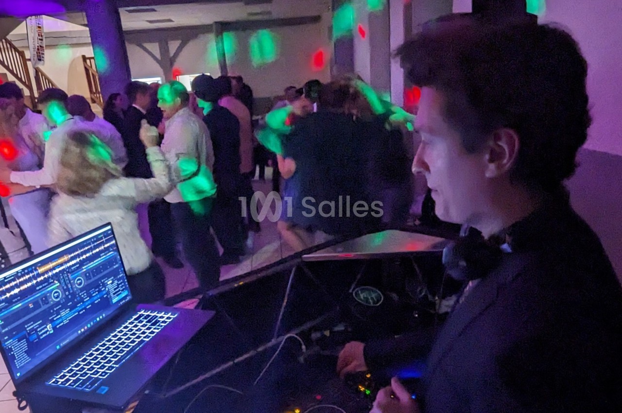 Un DJ mixe de la musique lors d'une soirée dansante avec des invités en train de danser sous des lumières colorées.