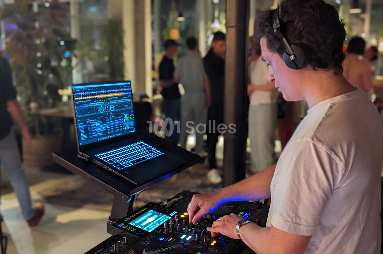 Un DJ mixe de la musique sur une console avec un ordinateur portable, dans un espace intérieur animé.