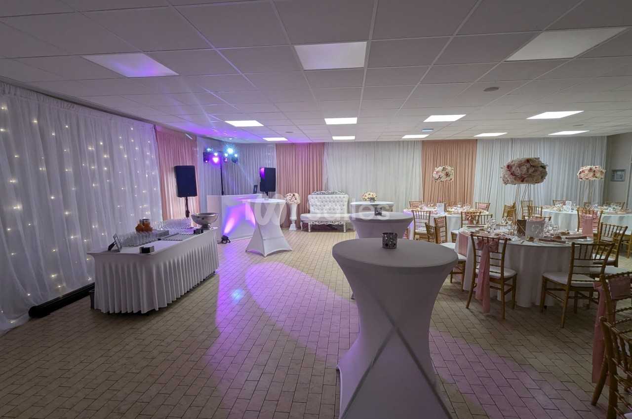 Salle de réception décorée avec des tables rondes, des chaises dorées, un buffet et un éclairage tamisé.