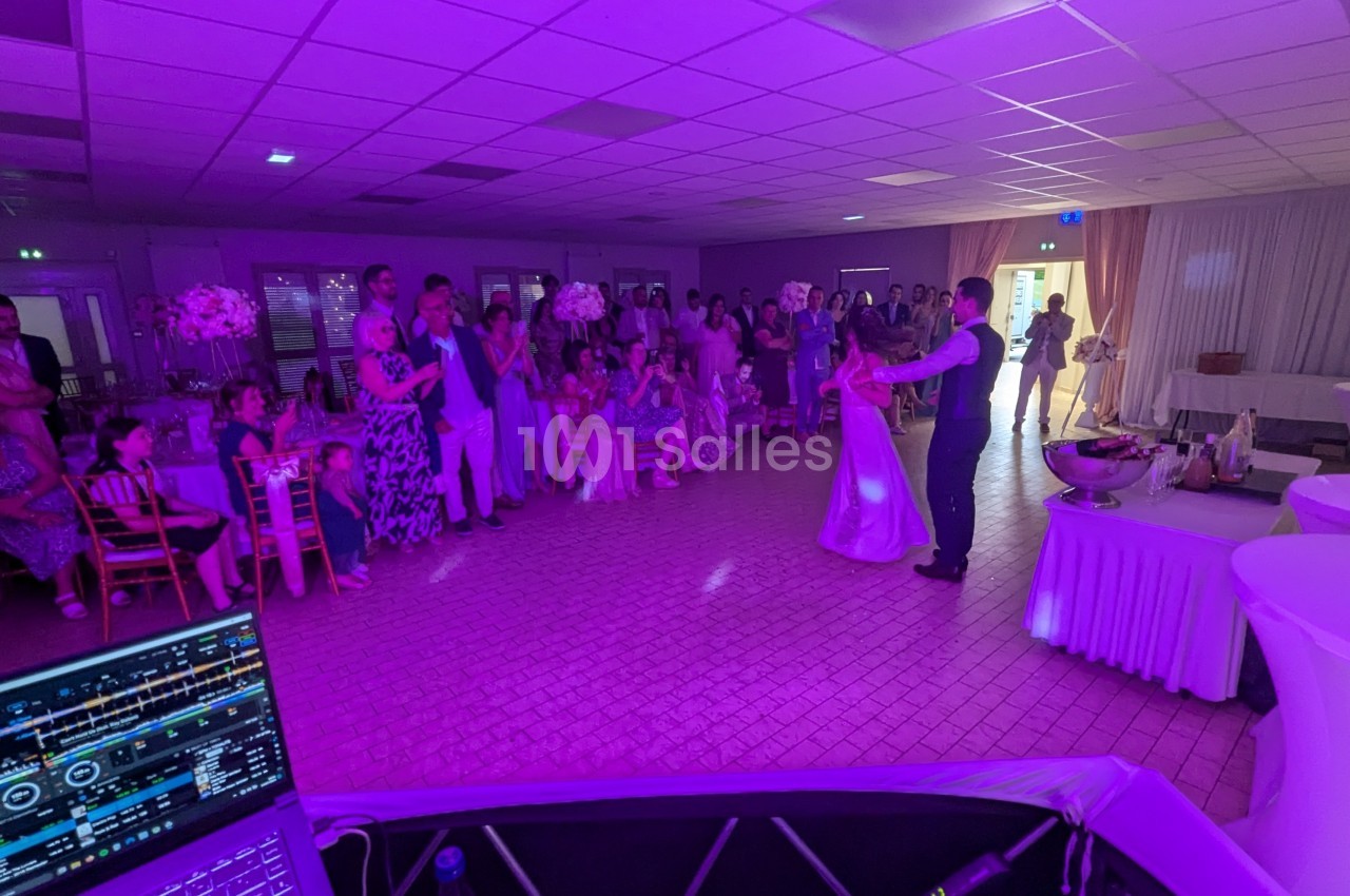 Un couple danse au centre d'une salle éclairée de lumières violettes, entouré d'invités assis et debout.
