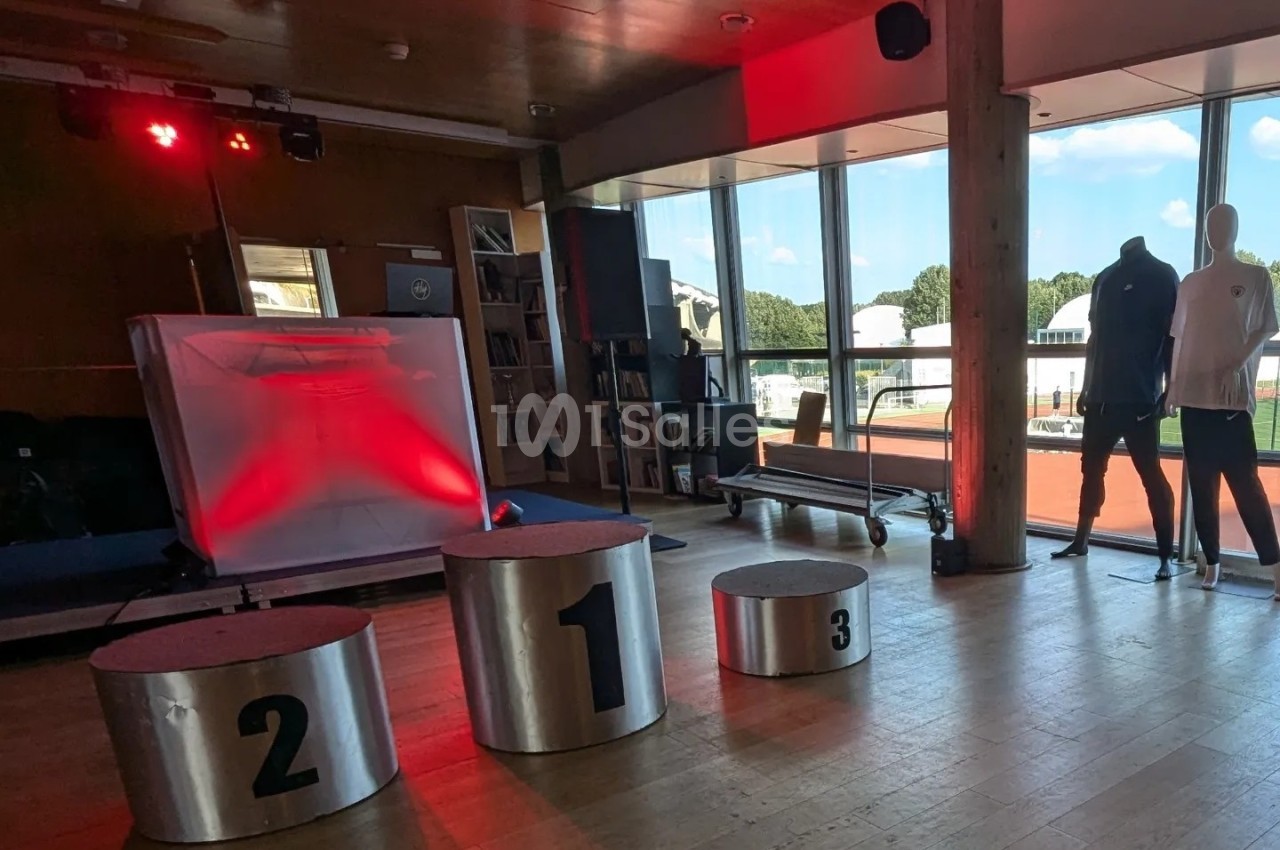 Salle lumineuse avec podiums numérotés, éclairage rouge, mannequins et vue sur l'extérieur à travers de grandes baies…