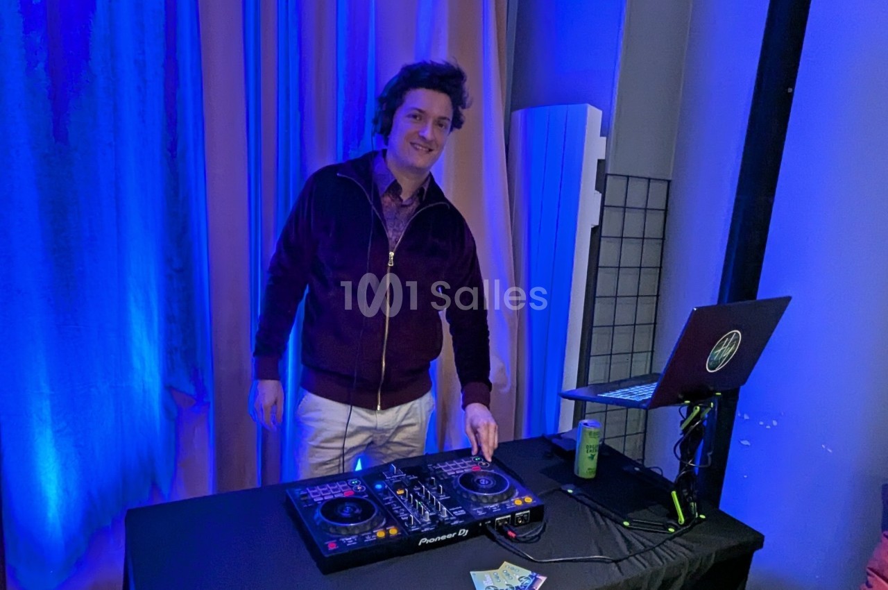 Un DJ souriant mixe de la musique sur une table de mixage dans un espace éclairé par des lumières bleues.