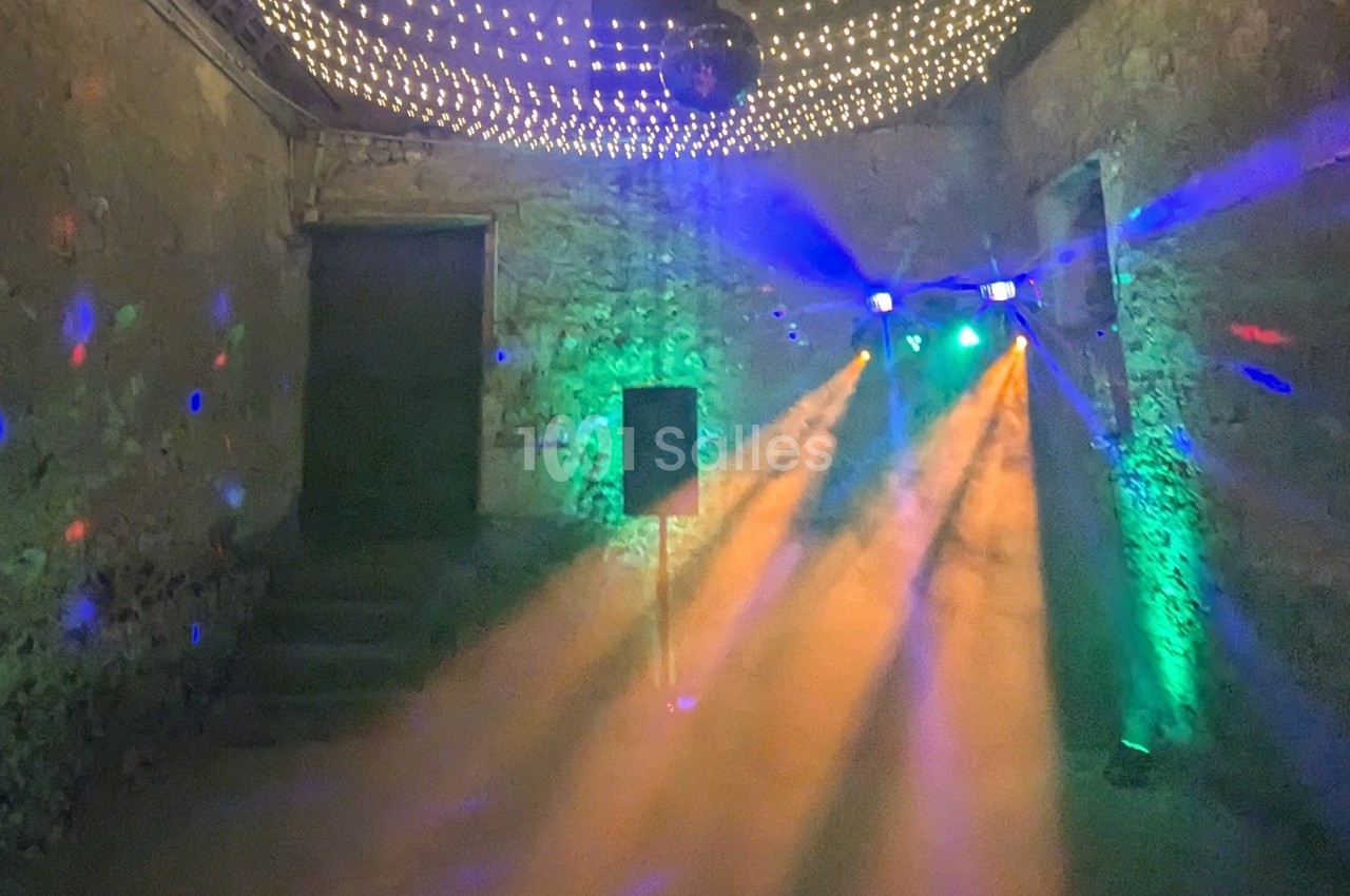 Salle en pierre avec éclairage coloré, projecteurs et fumée créant une ambiance festive.