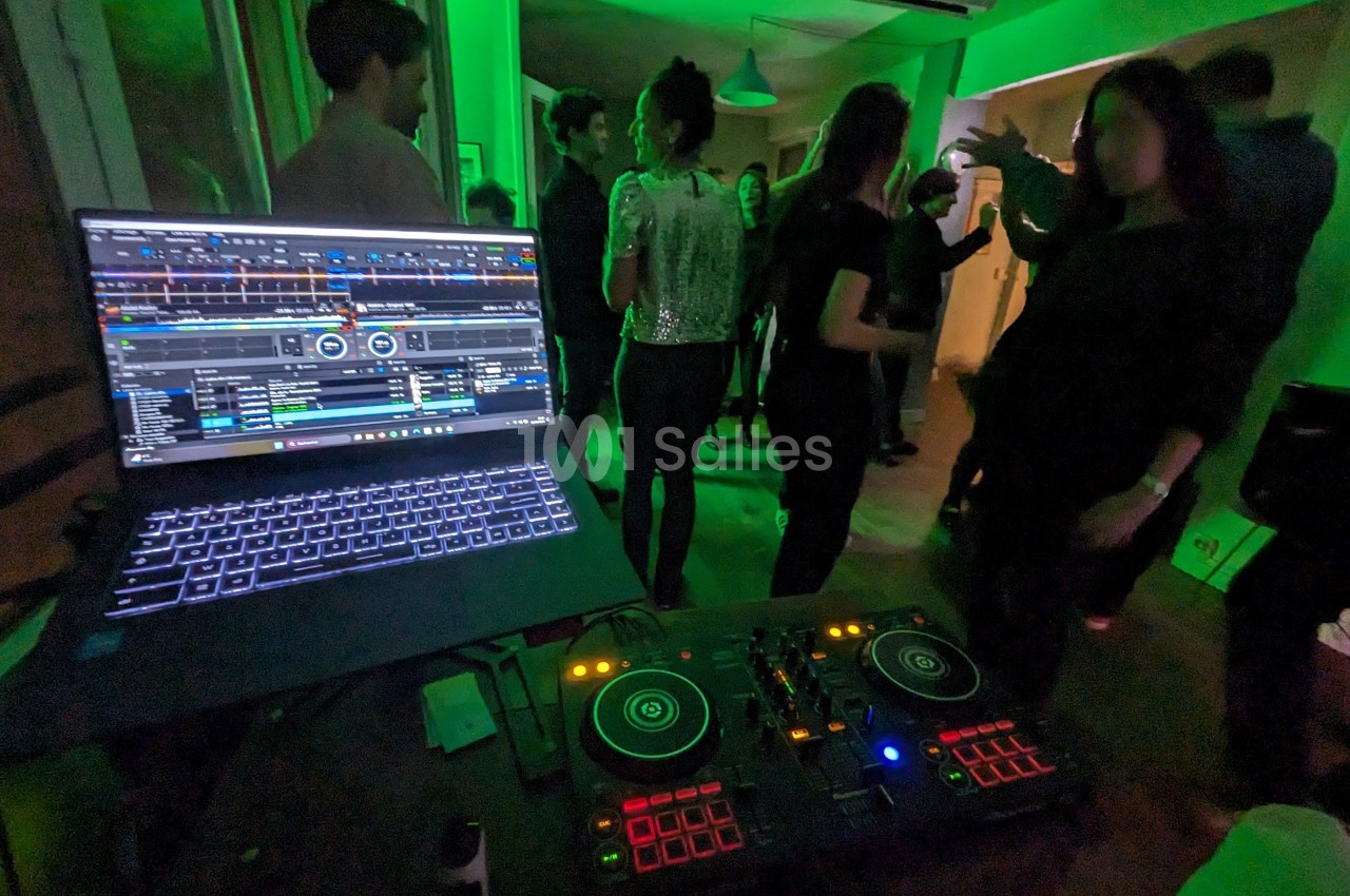 Des personnes dansent dans une pièce éclairée de lumières vertes, avec une table de mixage et un ordinateur au premier plan.