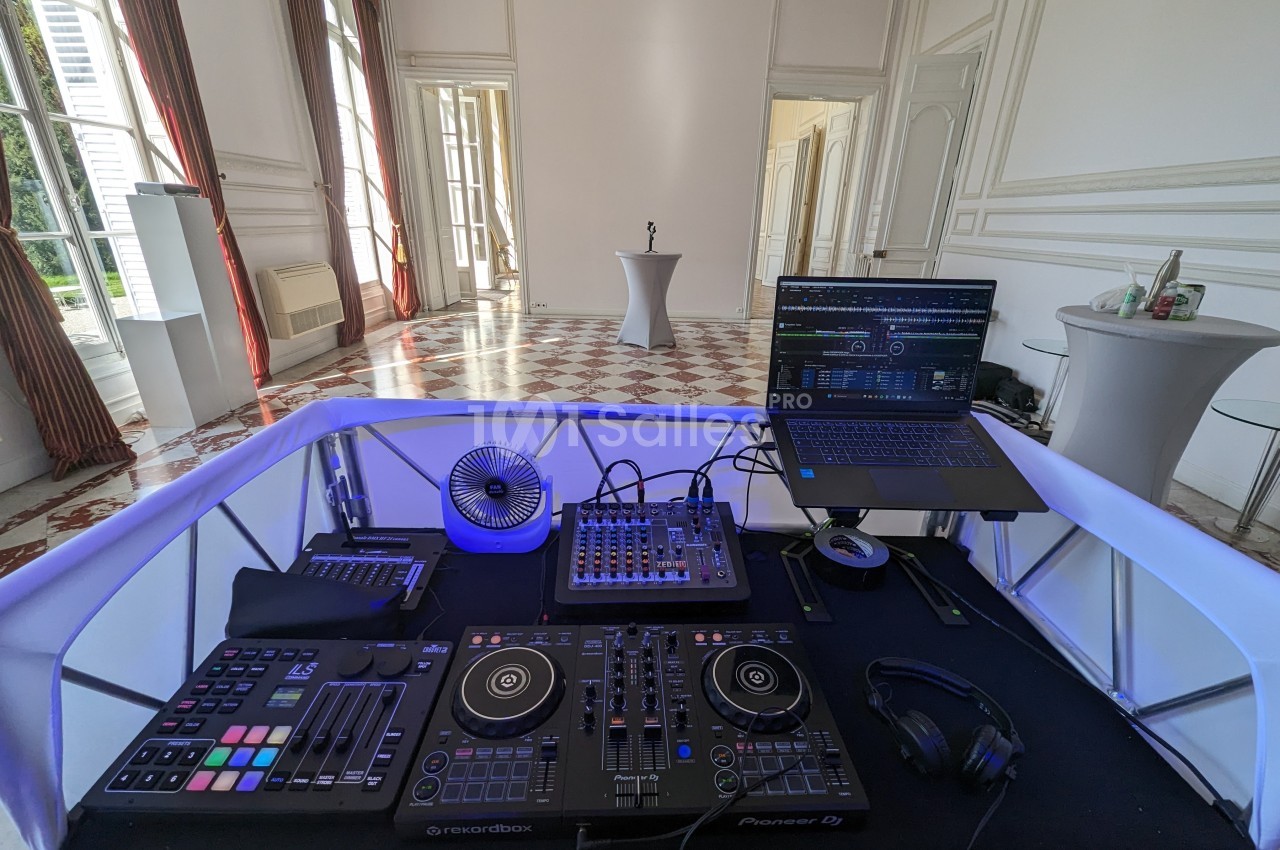 Poste de DJ avec platines, table de mixage, ordinateur portable et casque dans une salle lumineuse au sol carrelé.