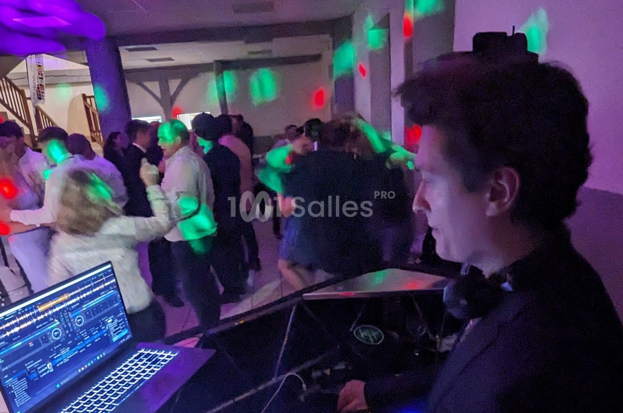Un DJ mixe de la musique lors d'une soirée dansante avec des invités sur une piste éclairée par des lumières colorées.