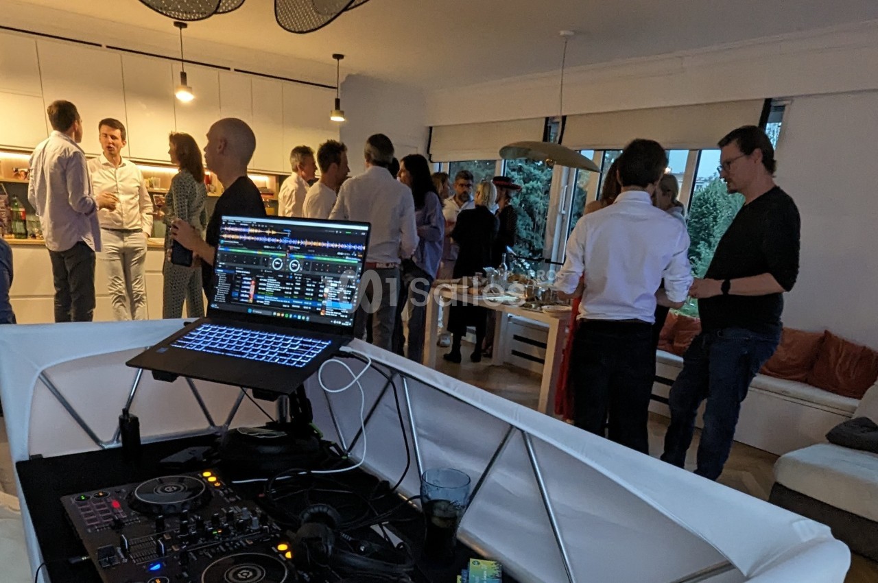 Vue d'une soirée conviviale avec des invités discutant dans un salon, un équipement de DJ visible au premier plan.