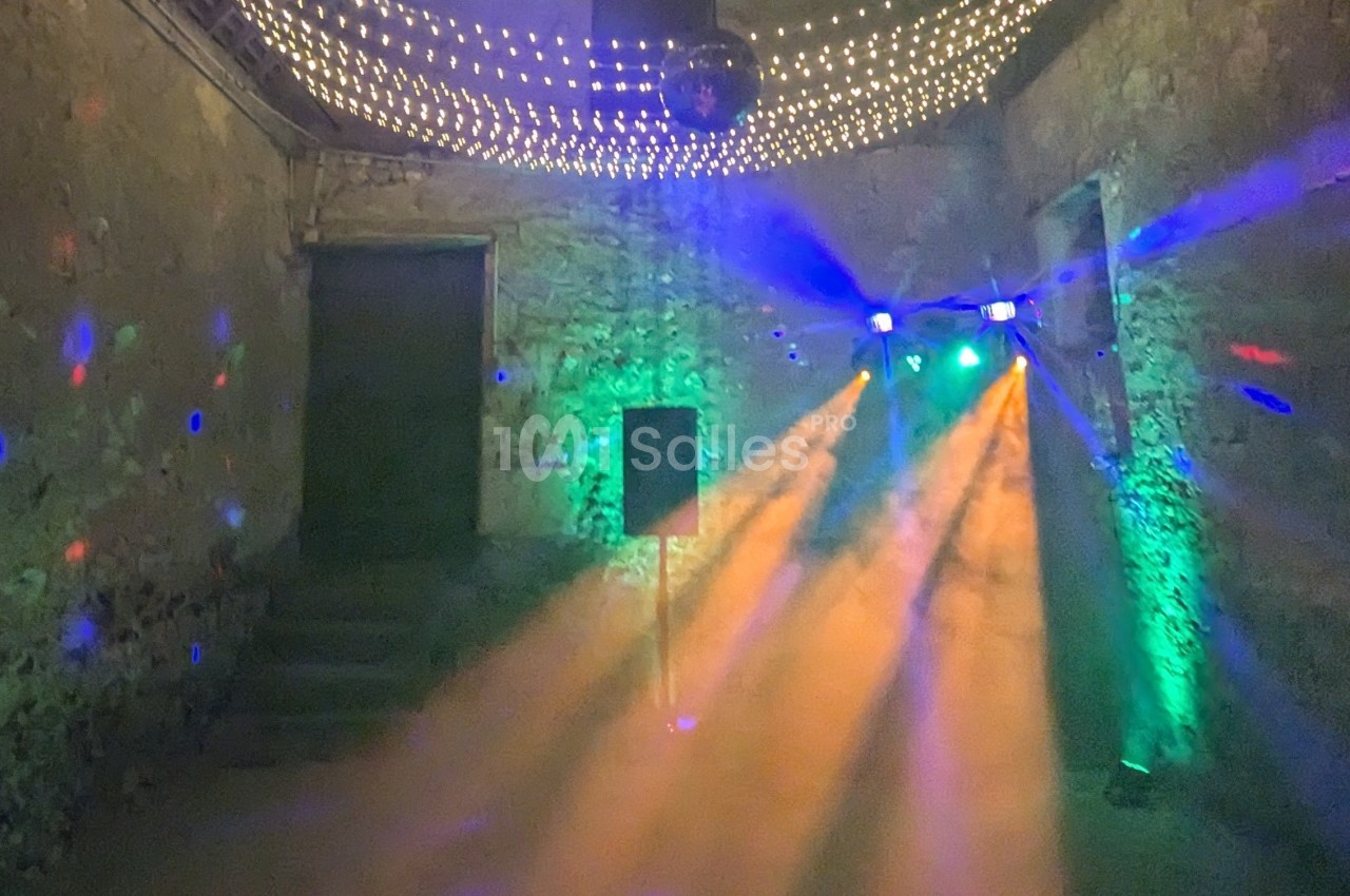 Salle en pierre avec éclairage coloré, jeux de lumière et machine à fumée créant une ambiance festive.