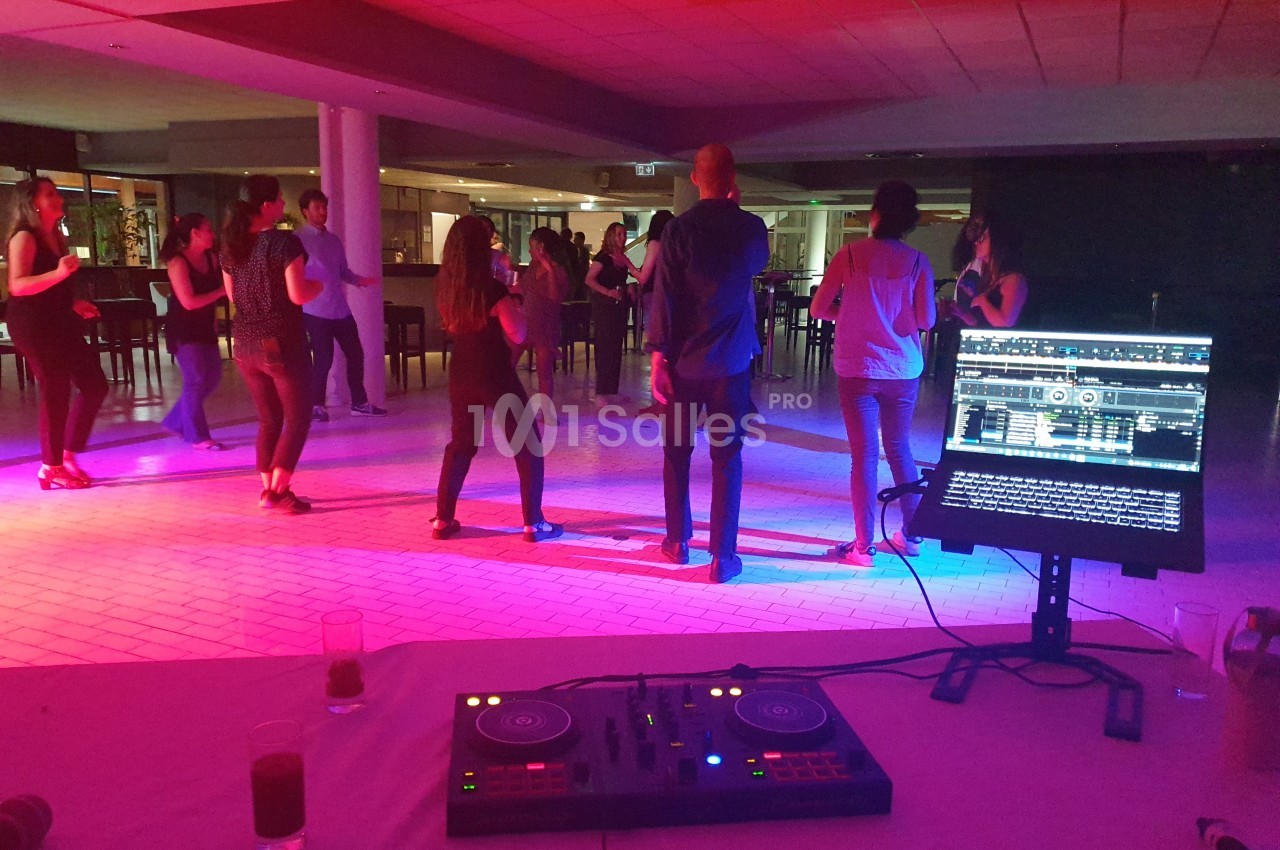 Des personnes dansent en groupe sous des lumières colorées, avec une table de mixage et un écran au premier plan.