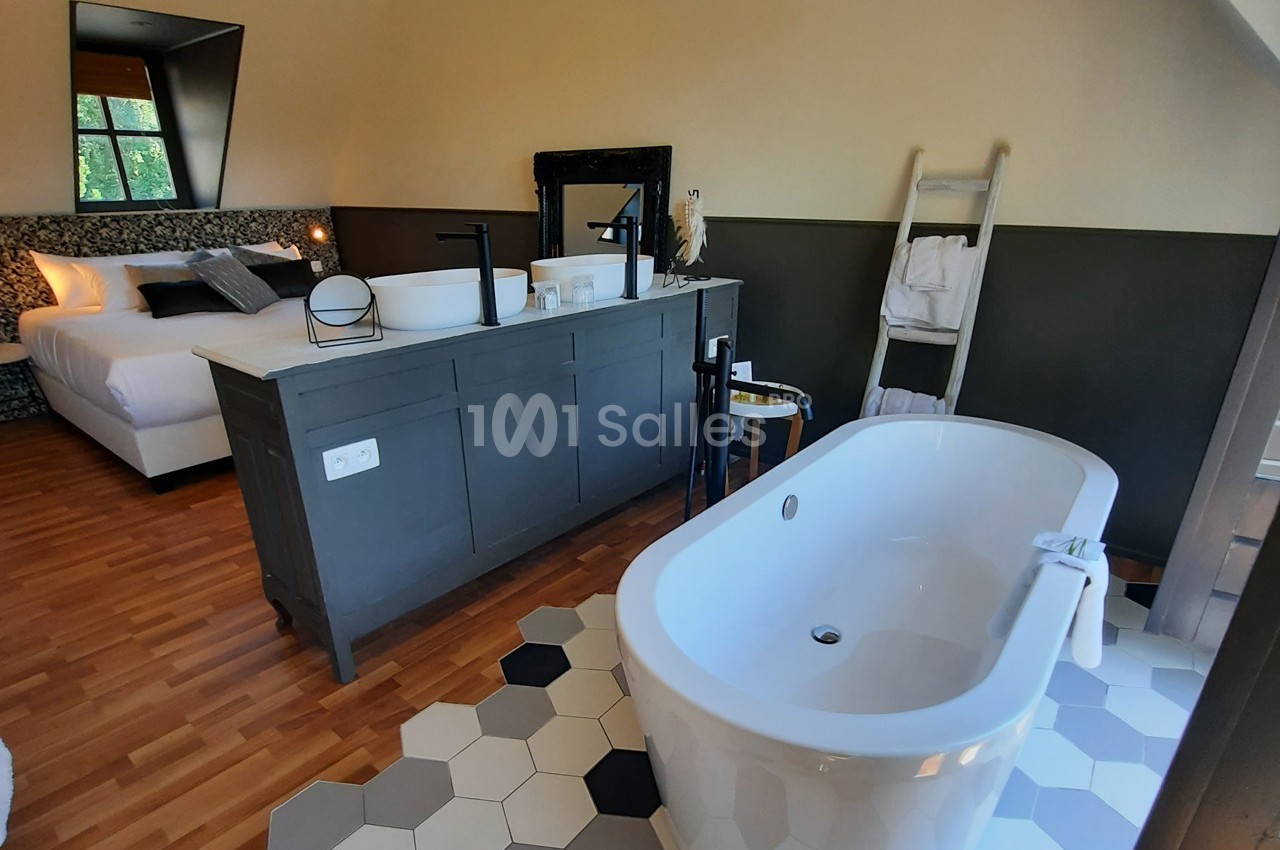 Chambre avec lit double, baignoire îlot, parquet, carrelage hexagonal et échelle porte-serviettes.