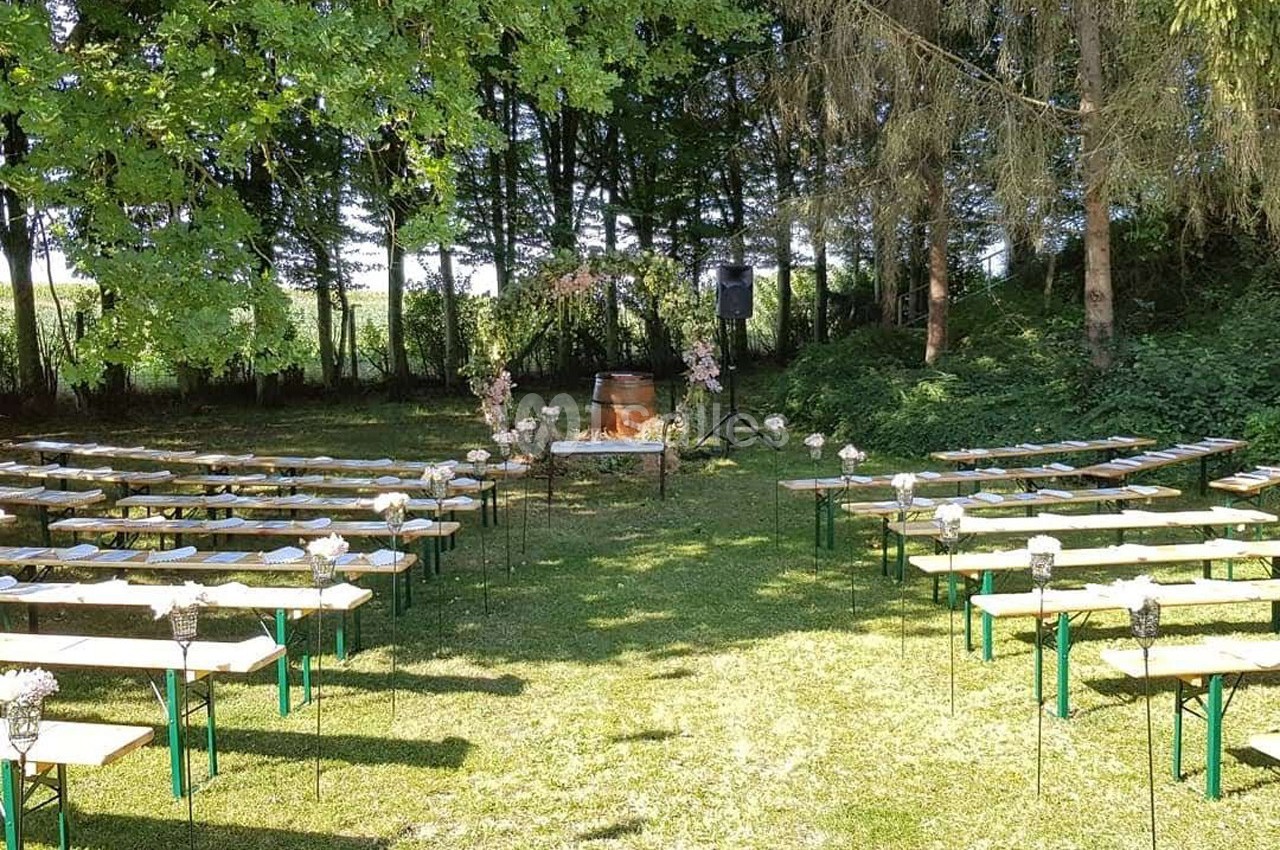 Disposition de bancs en bois et métal dans un espace extérieur verdoyant, avec une arche florale au centre.