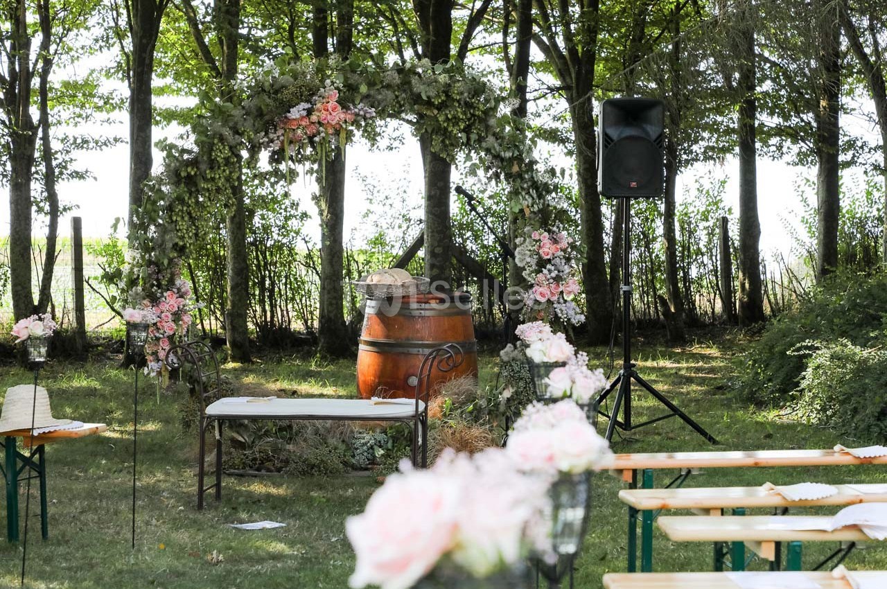 Arche fleurie et tonneau décoratif dans un cadre boisé, entourés de bancs pour une cérémonie en plein air.
